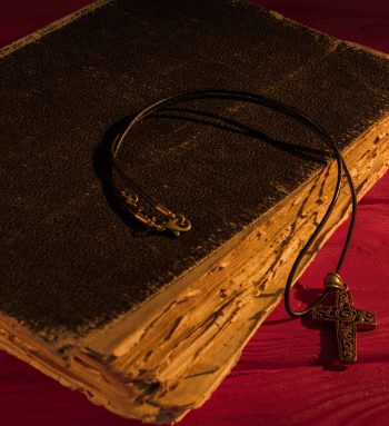 Very old ancient holy bible and neckalce cross. Worn vintage retro book on red wood.