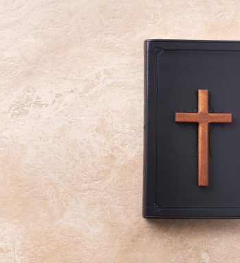 Wooden cross on Bible over marble background. Reminder of Jesus sacrifice and Christ resurrection. Easter passover. Eucharist concept. Christianity symbol and faith.